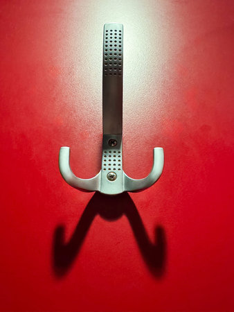 Silver metal wall hook on red background creating shadow.
