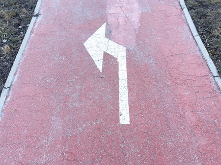 Worn red asphalt path with left turn arrow and cracked surface.の写真素材