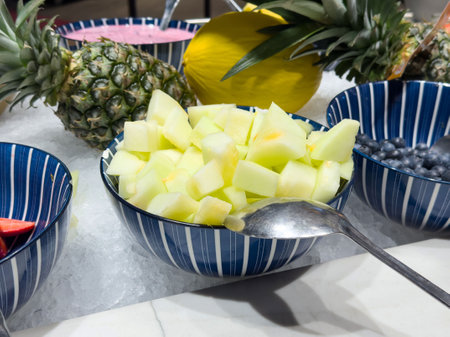 Fresh fruit dessert display with pineapple, blueberries, and honeydew melon cubes in striped bowls.の写真素材