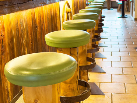 Rustic bar interior with wooden stools and green cushions in cozy warm setting.の写真素材