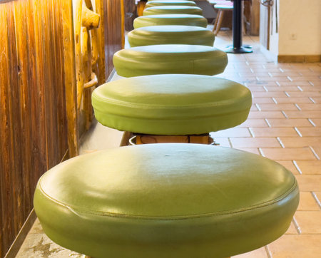 Row of green bar stools in rustic indoor setting with tiled floor.の写真素材