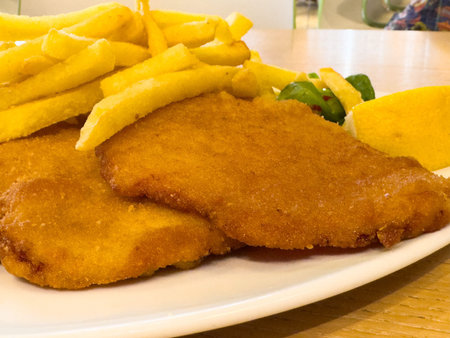 Crispy schnitzel and fries with lemon and bell peppers on a white plate.