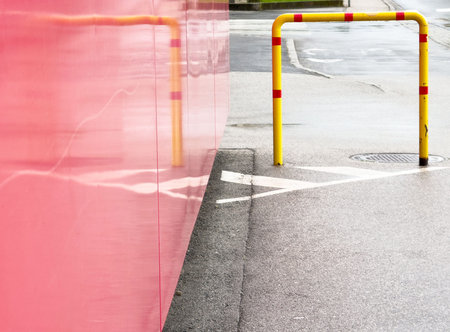Urban scene with red wall, wet pavement, and yellow safety rail on rainy day.の写真素材