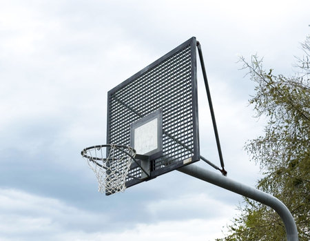 Outdoor metal basketball hoop against cloudy sky.