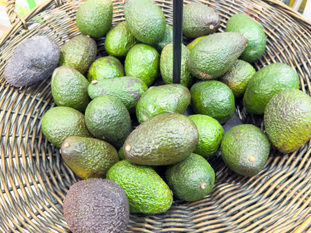 Fresh green and ripe black avocados in wicker basket display at market.