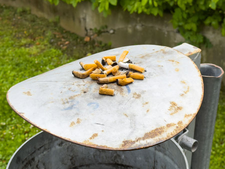 Cigarette butts on metal trash lid in urban outdoor setting.の写真素材
