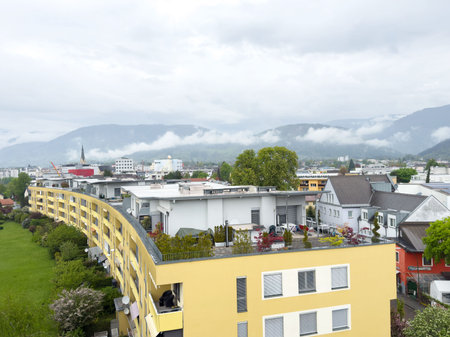 Aerial view of urban residential area with yellow apartment buildings and cloudy mountain backdrop.の写真素材