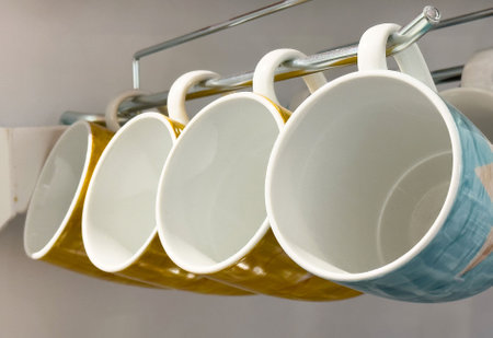 Colorful ceramic mugs hanging on rack in kitchen detail close-up.の写真素材