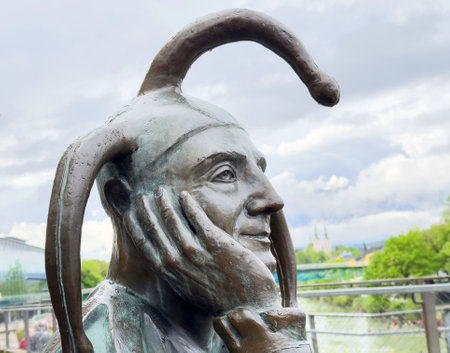 Bronze jester sculpture with amused expression against cloudy sky.の写真素材