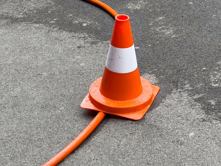 Orange traffic cone on wet asphalt with cable passing through base.の写真素材