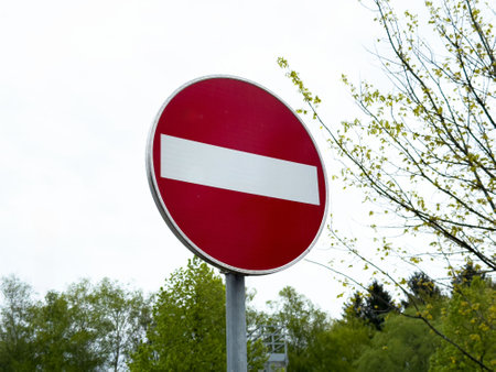 Red and white no entry road sign against tree line and sky background.の写真素材