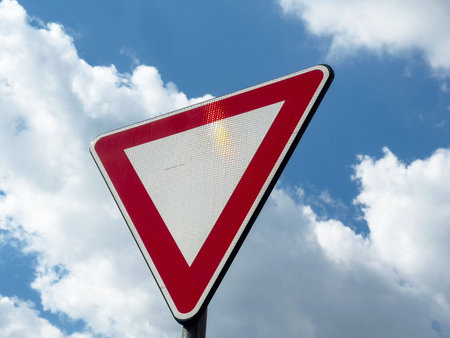 Red and white yield sign against a cloudy blue sky.