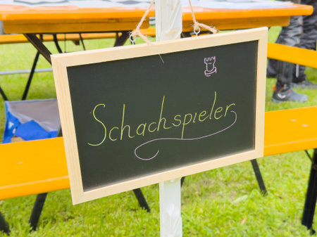 Outdoor chess event chalkboard sign on green lawn with tables and chairs.の写真素材