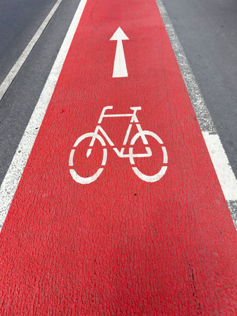 Red bicycle lane with arrow symbol on urban roadway.の写真素材