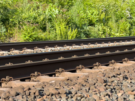 Railway tracks with gravel and lush greenery on a sunny day.の写真素材
