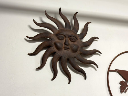 Rustic metal sun sculpture on white wall with expressive facial features.の写真素材