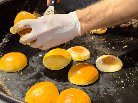 Hands preparing golden buns on griddle outdoors.の写真素材
