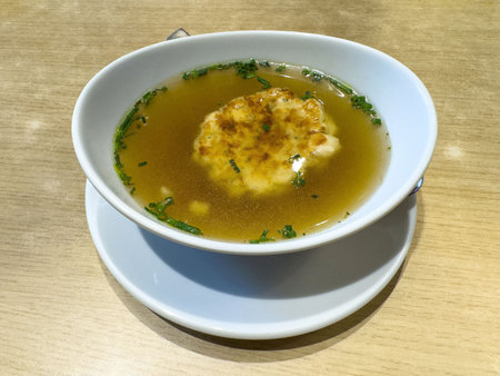 Delicious clear broth soup with herb and dumpling garnish on wooden table.の写真素材