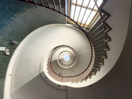 Spiral staircase with red railing and natural light from above.