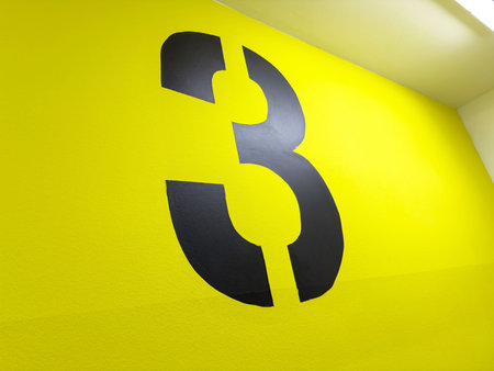 Bold black number three on vibrant yellow wall in modern interior design.