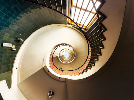 Spiral staircase with green tiled wall and natural light from window.