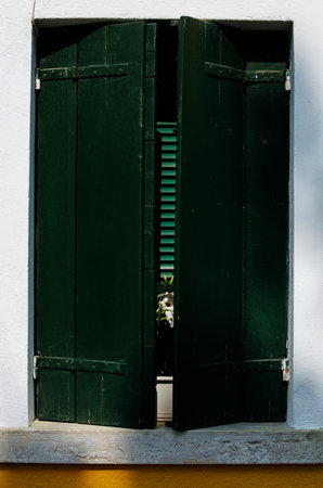 Partially open dark green wooden window on white wall with yellow trim.の写真素材