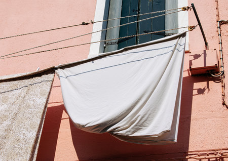 White sheet hanging on clothesline against pink wall.の写真素材