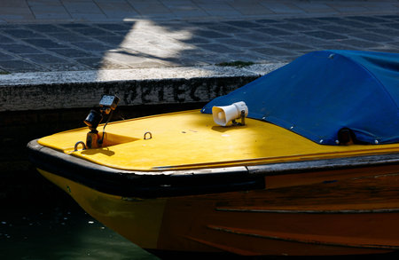 Yellow boat with blue cover docked by stone walkway in sunlight.の写真素材