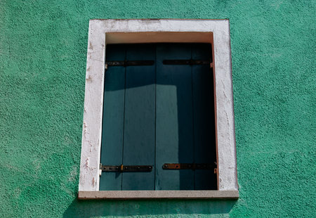 Closed wooden shuttered window on green stucco wall.の写真素材