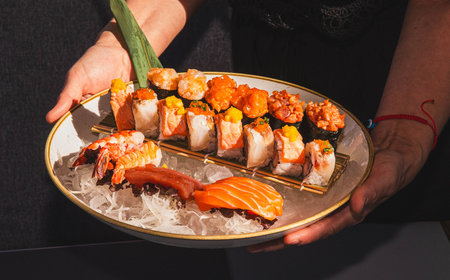 Assorted sushi platter with lobster and salmon garnish held by female hands.