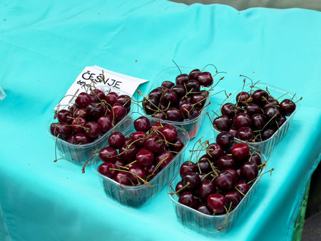 Fresh dark cherries in clear containers on teal tablecloth at market.の写真素材