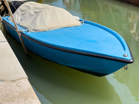 Blue wooden boat with beige cover docked on calm water canal.の写真素材