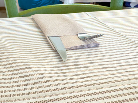 Neatly arranged cutlery on striped tablecloth with green chair in background.の写真素材