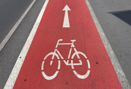 Red bike lane with white arrow on asphalt road.の写真素材