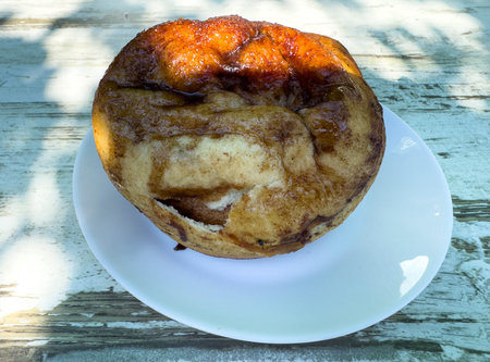 Sweet glazed cinnamon bread on white plate under sunlight.