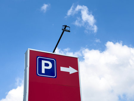 Parking sign with arrow on red background under clear blue sky.の写真素材