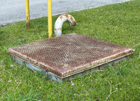 Rusty access hatch on green grass with metal pipe and yellow poles.の写真素材