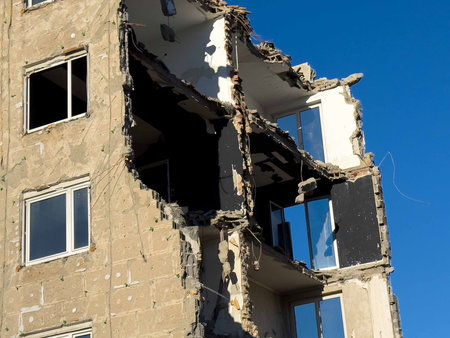 Partially collapsed building with exposed interiors against clear blue sky.
