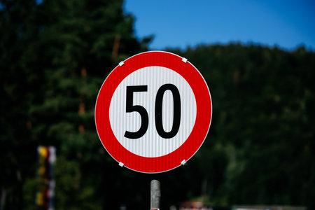 Speed limit sign with 50 in red circle against green forest background.の写真素材