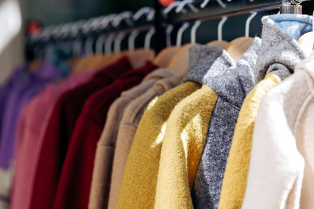 Colorful array of cozy sweaters hanging on a rack in sunlight.の写真素材