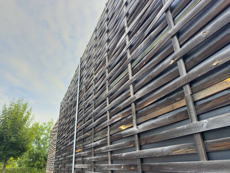 Modern wooden slatted fence in outdoor urban landscape with cloudy sky.の写真素材