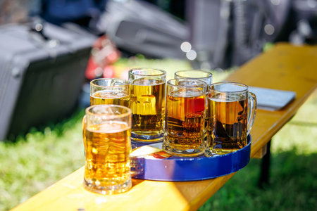 Assorted beer mugs on outdoor wooden table in sunlit garden setting.