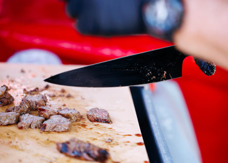 Chef slicing grilled beef on cutting board at outdoor bbq event.