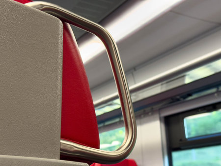 Modern train interior with red seats and sleek metal handrails.
