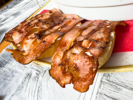 Crispy cooked bacon slices on bread on a red cutting board.