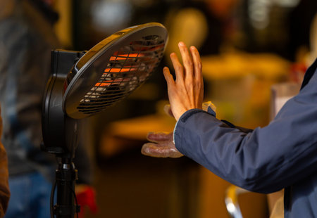 Close-up of person warming hands near electric heater indoors on a cold day.の写真素材