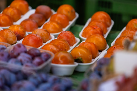 Fresh persimmons and plums on display at an outdoor market stall.の写真素材