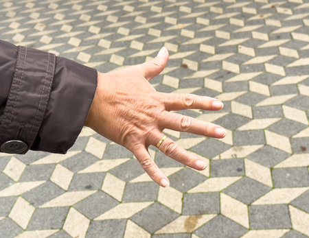 Caucasian adult female hand with ring on geometric paved surface.の写真素材