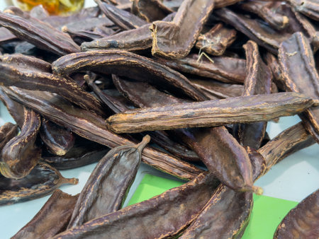 Dried carob pods displayed for sale on a market stand.