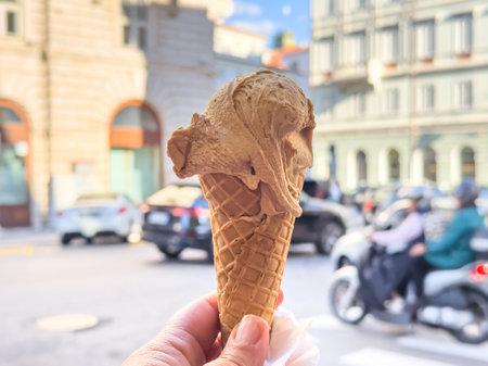 Hand holding delicious ice cream cone on busy city street.